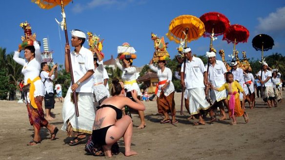 246627-balinese-dressed-in-traditional-clothing-walk-on-a-beach-past-tourists-during-a-melasti-ceremony-prayer-at-kuta-in-denpasar